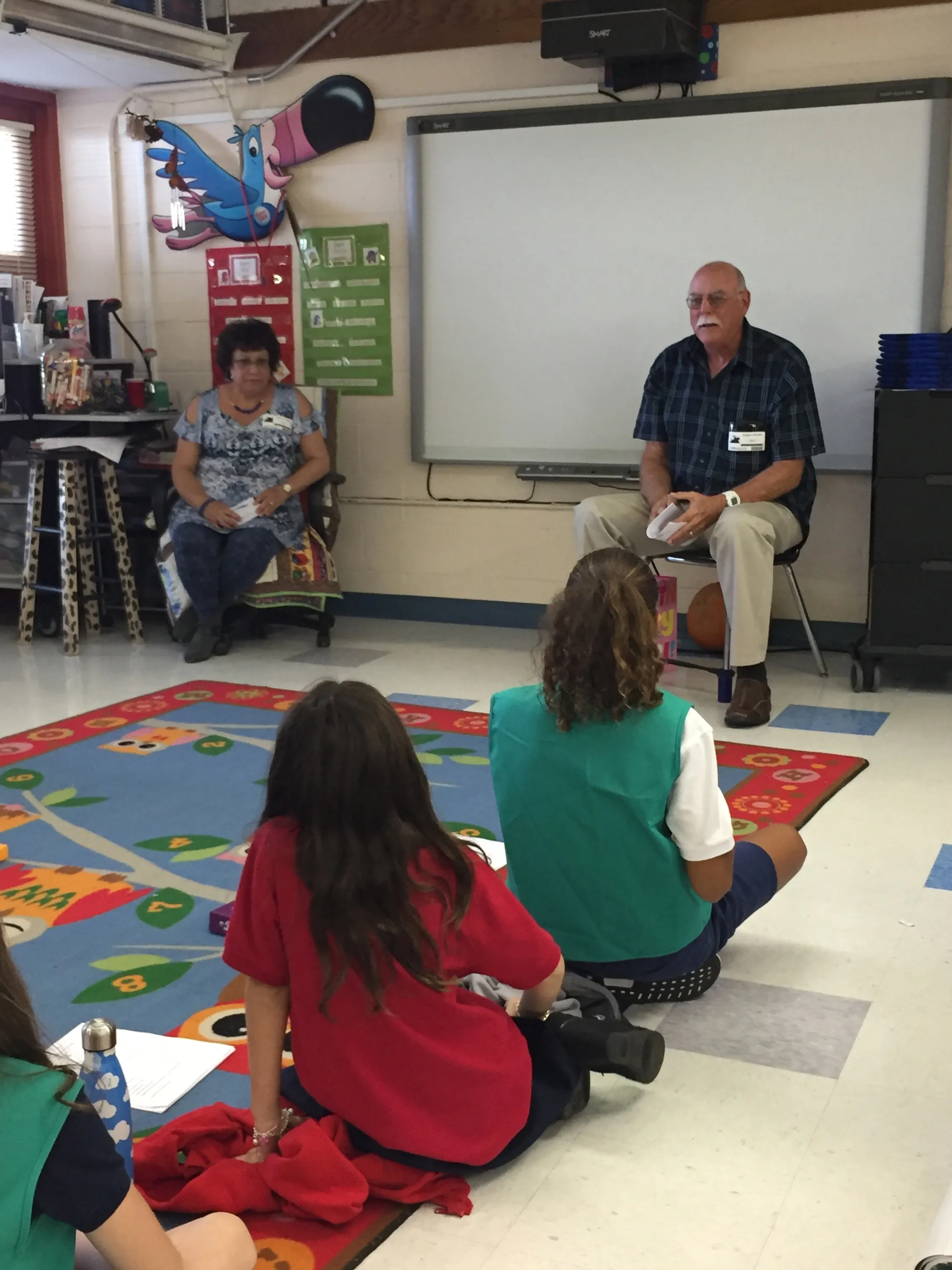A group of people are sitting on the floor in front of a white board