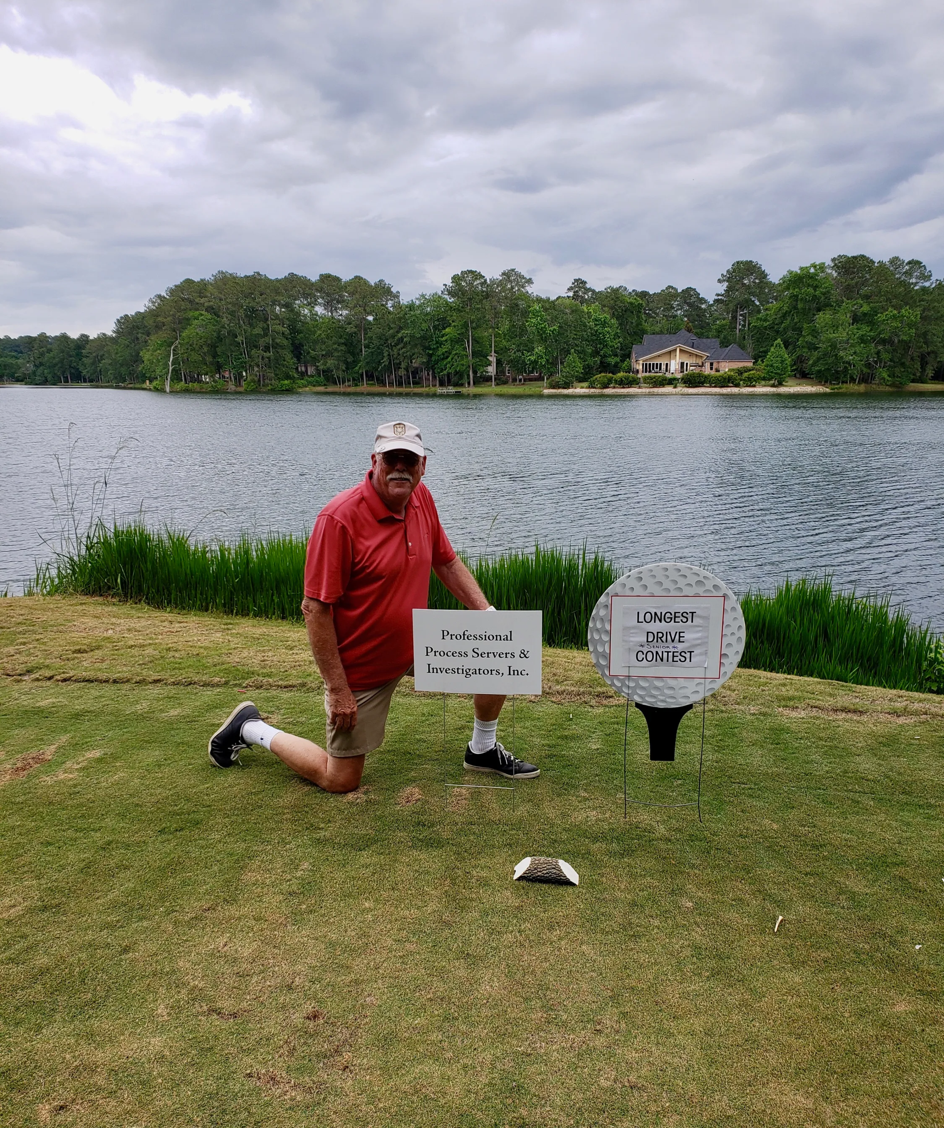 A man is kneeling on a golf course holding a sign.