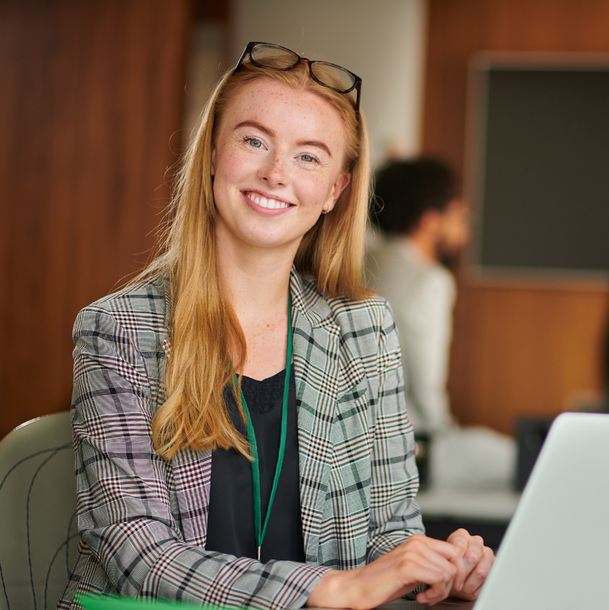 A woman is sitting in front of a laptop computer and smiling.
