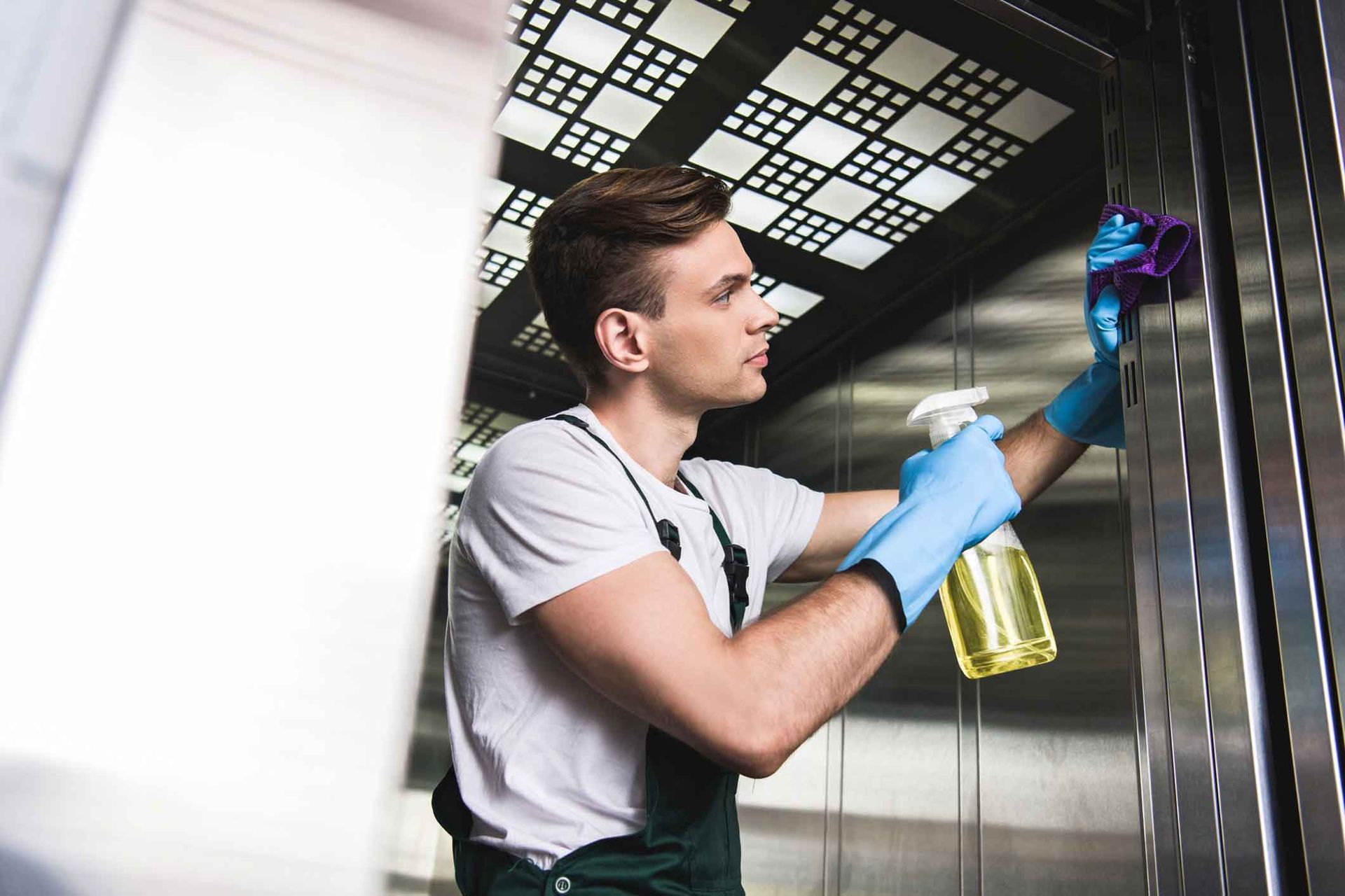 A man is cleaning an elevator with a sponge and spray bottle.