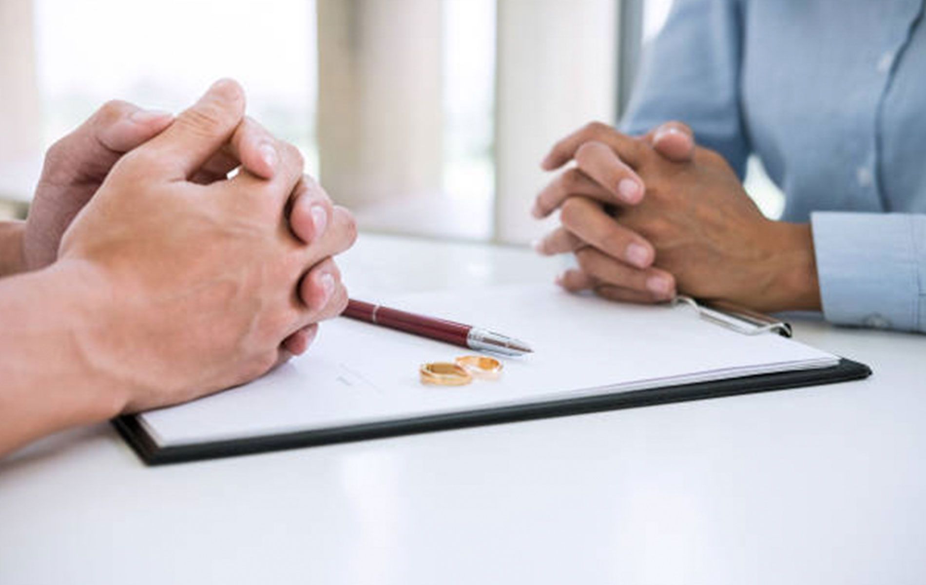 A man and a woman are sitting at a table with their hands folded.