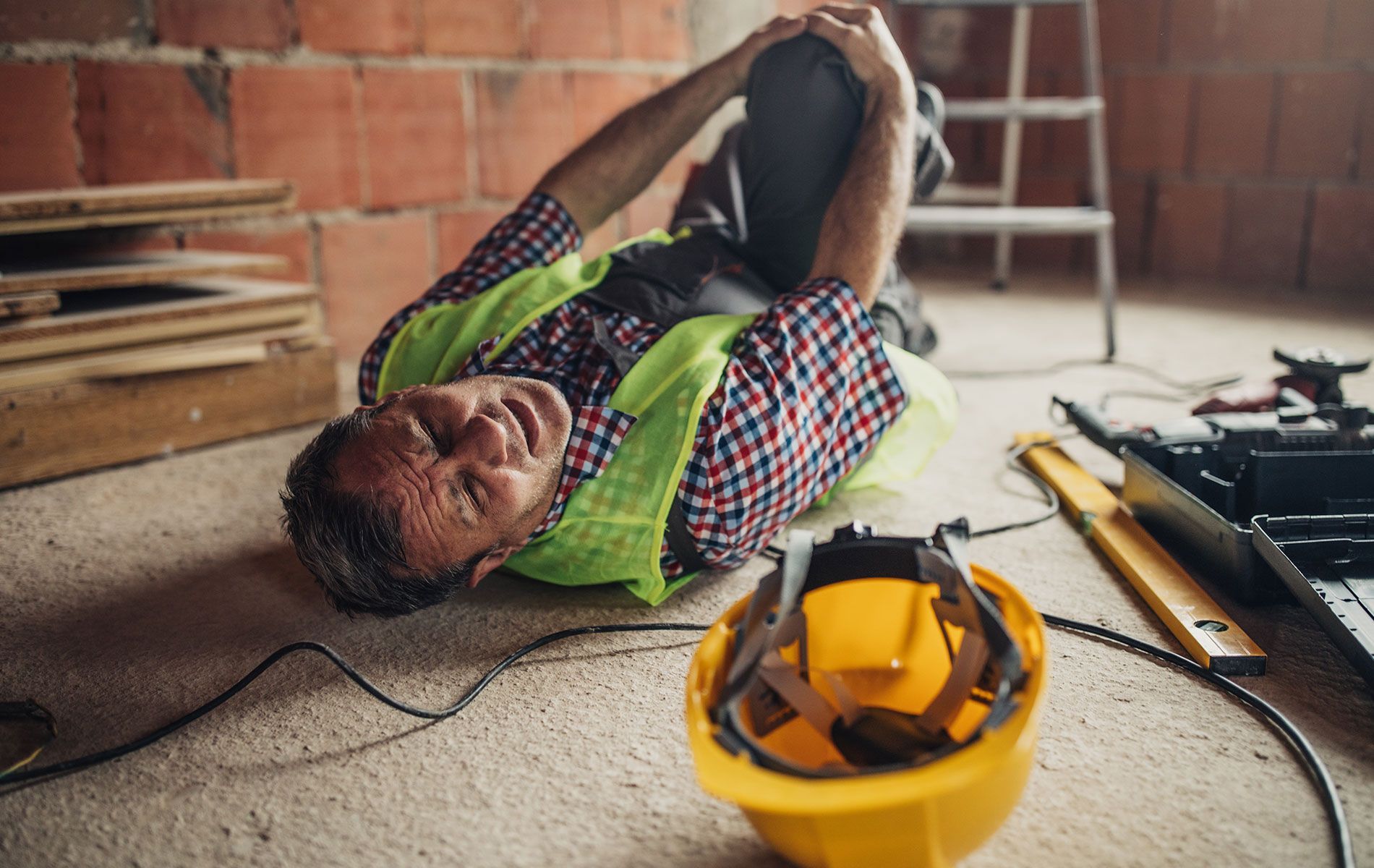 A construction worker is laying on the floor with his knee in pain.