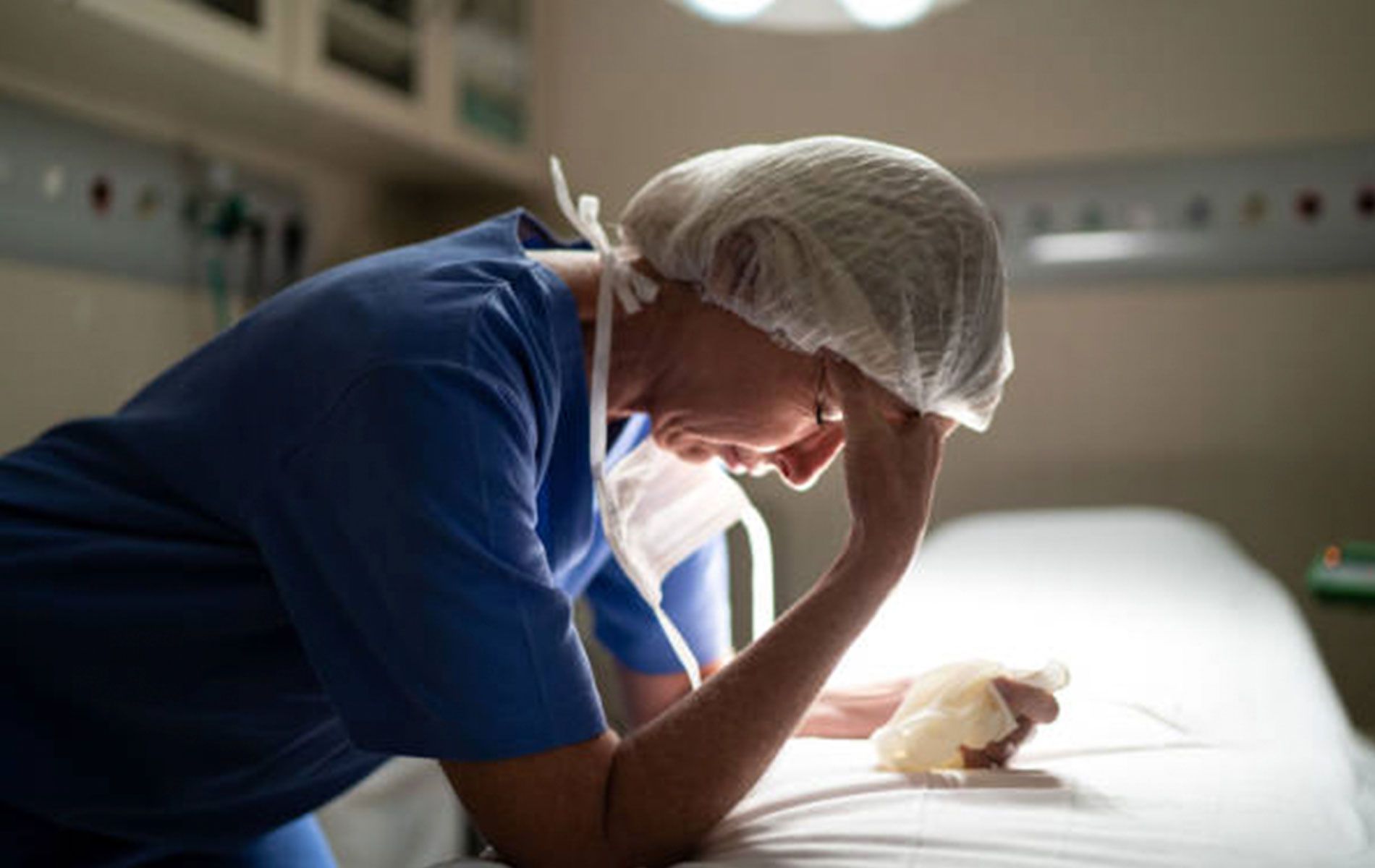 A nurse is sitting on a hospital bed with her head in her hands.