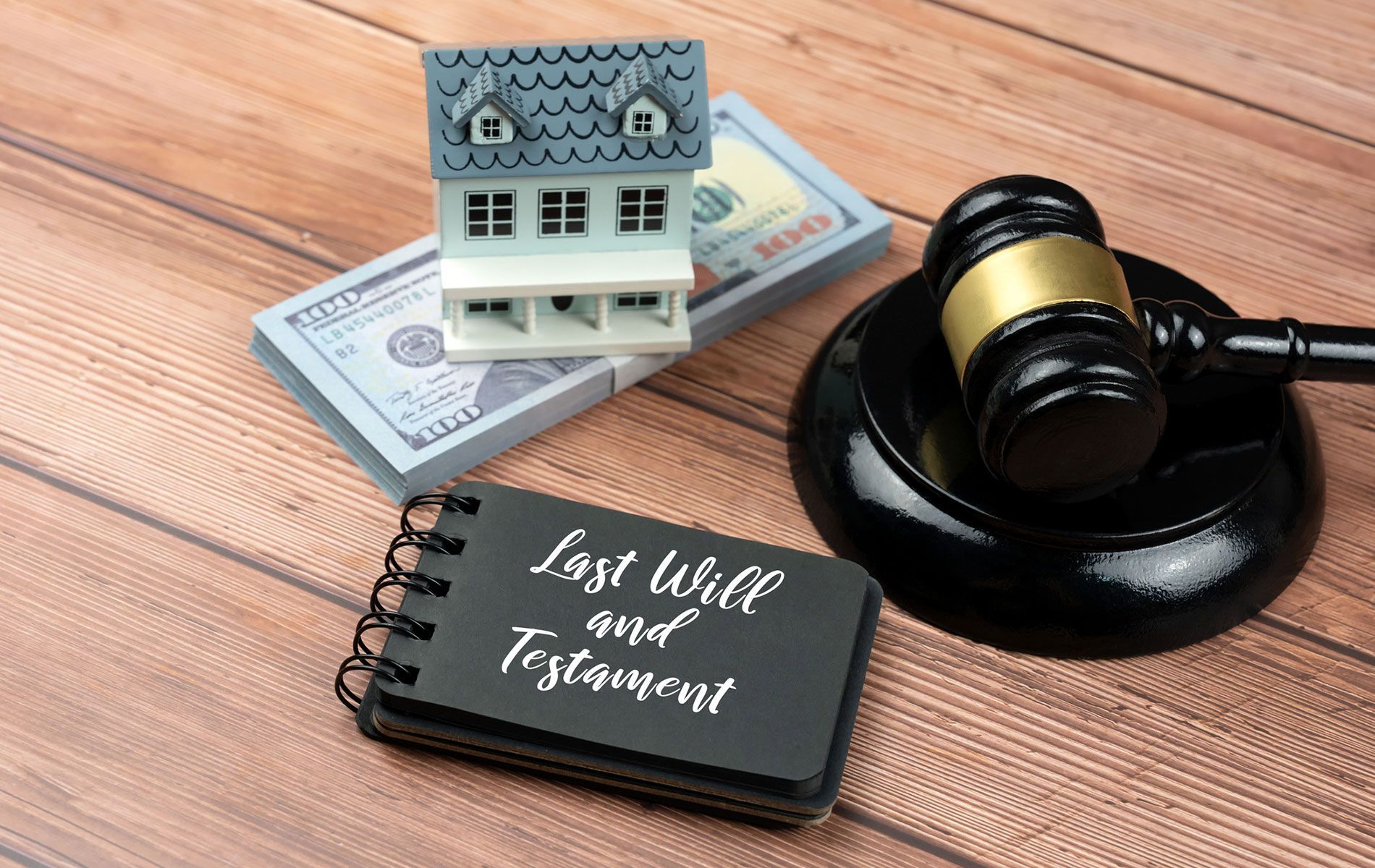 A judge 's gavel , a book of last will and testament , and a model house on a wooden table.