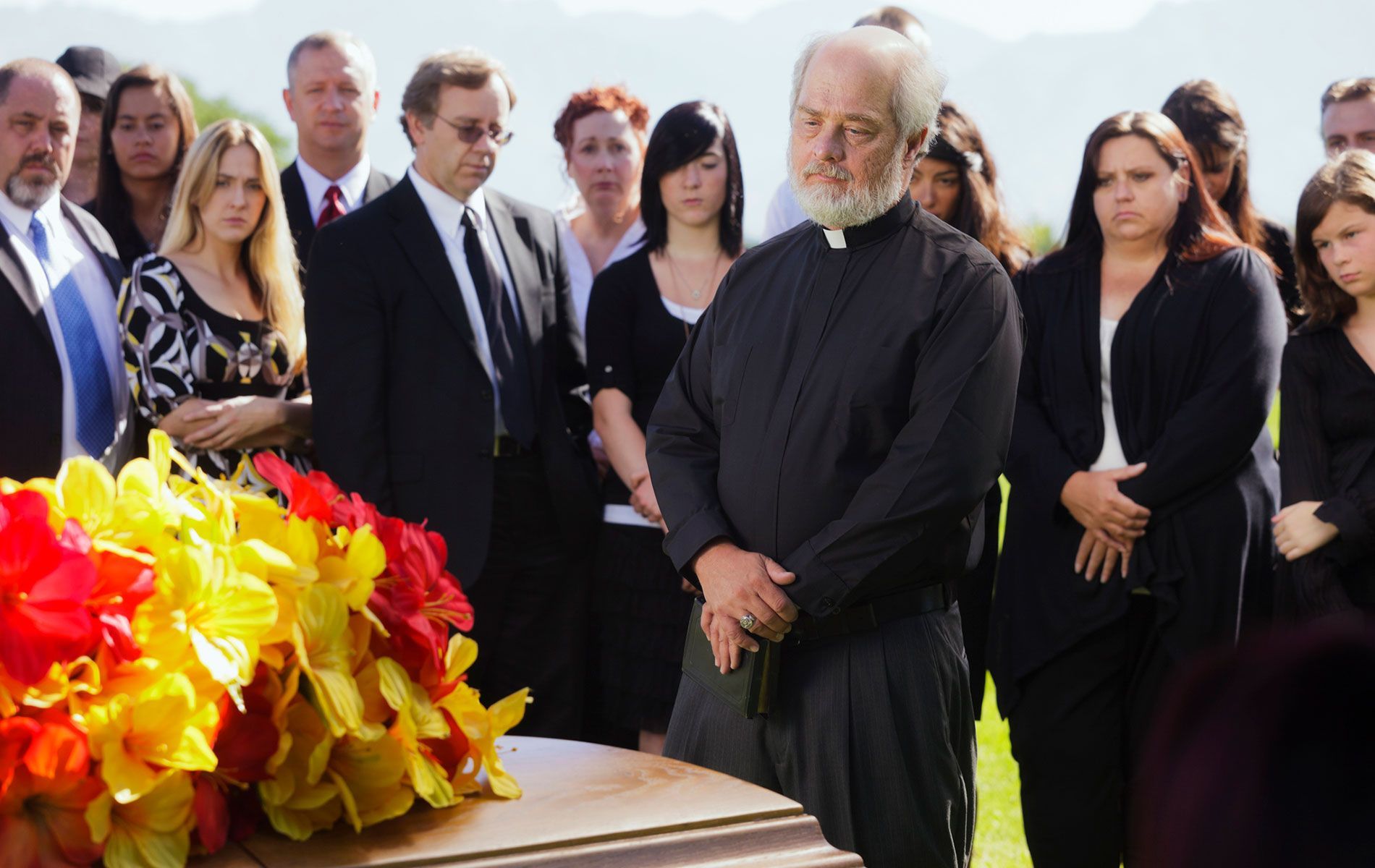 A group of people standing around a coffin with flowers on it