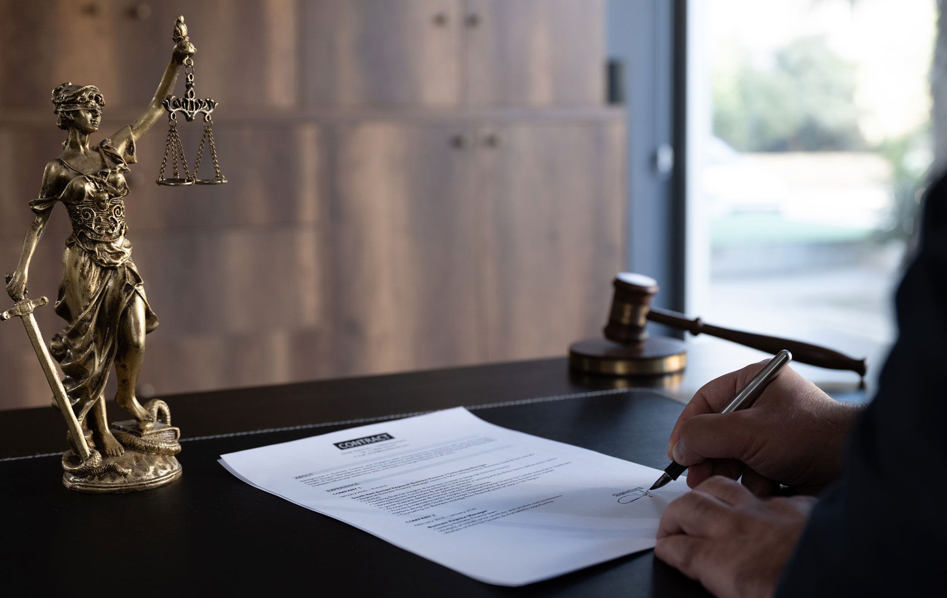 A person is writing on a piece of paper in front of a statue of justice.