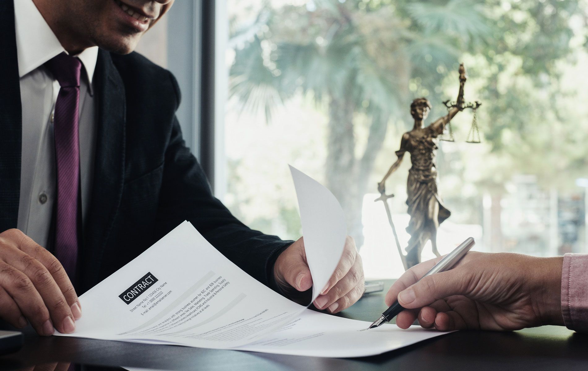 A man in a suit and tie is signing a document in front of a statue of justice.