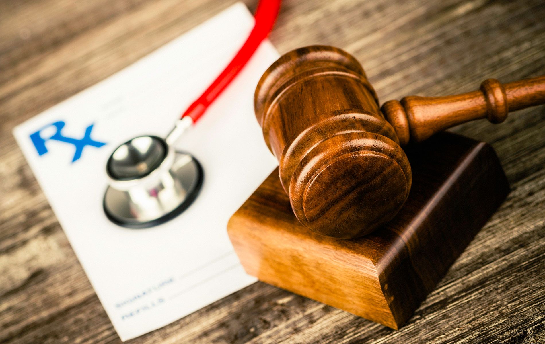 A wooden gavel is sitting on a wooden table next to a stethoscope and a prescription.