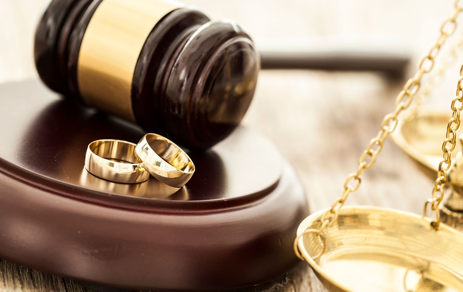 A pair of wedding rings sitting on top of a wooden gavel next to a scale.