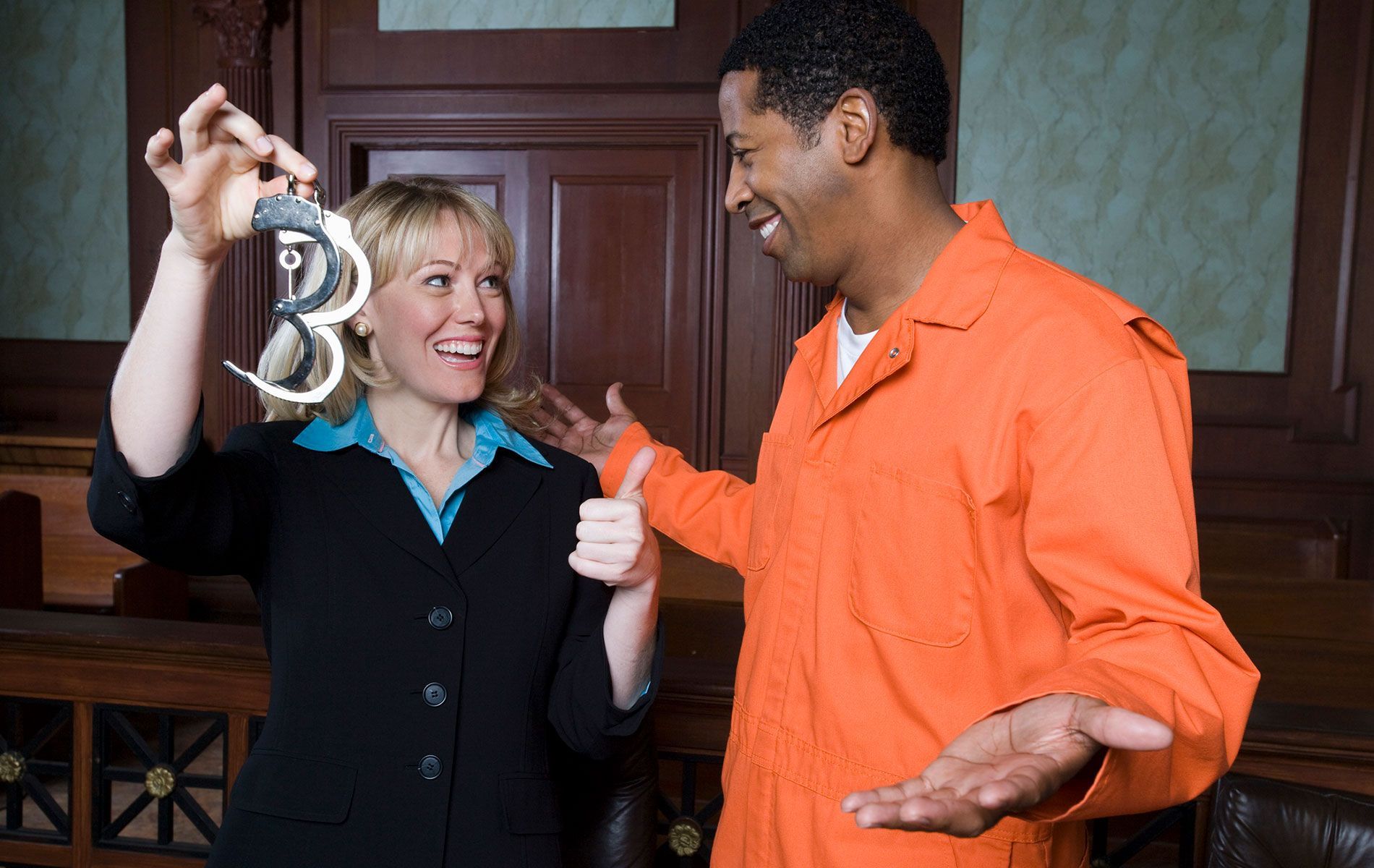 A woman is holding a pair of handcuffs next to a man in an orange jumpsuit.