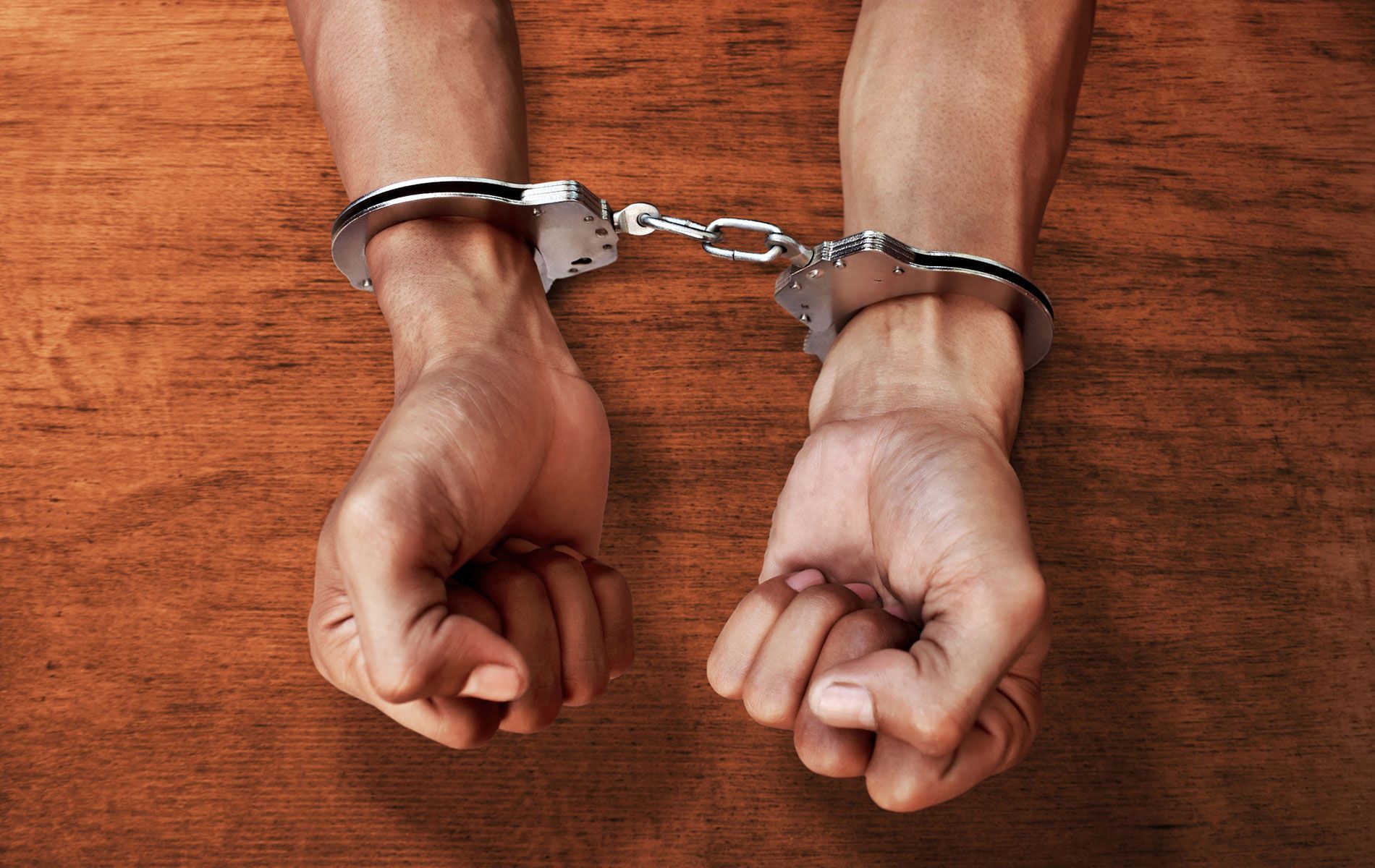 A man in handcuffs is sitting at a wooden table.