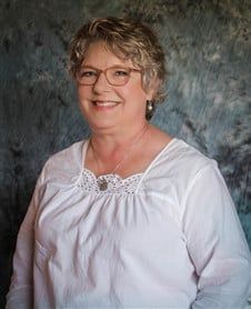 a woman wearing glasses and a white shirt is smiling for the camera .