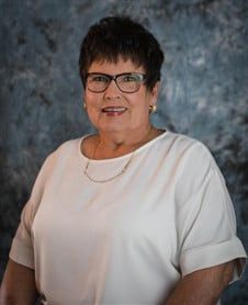 a woman wearing glasses and a white shirt is smiling for the camera .