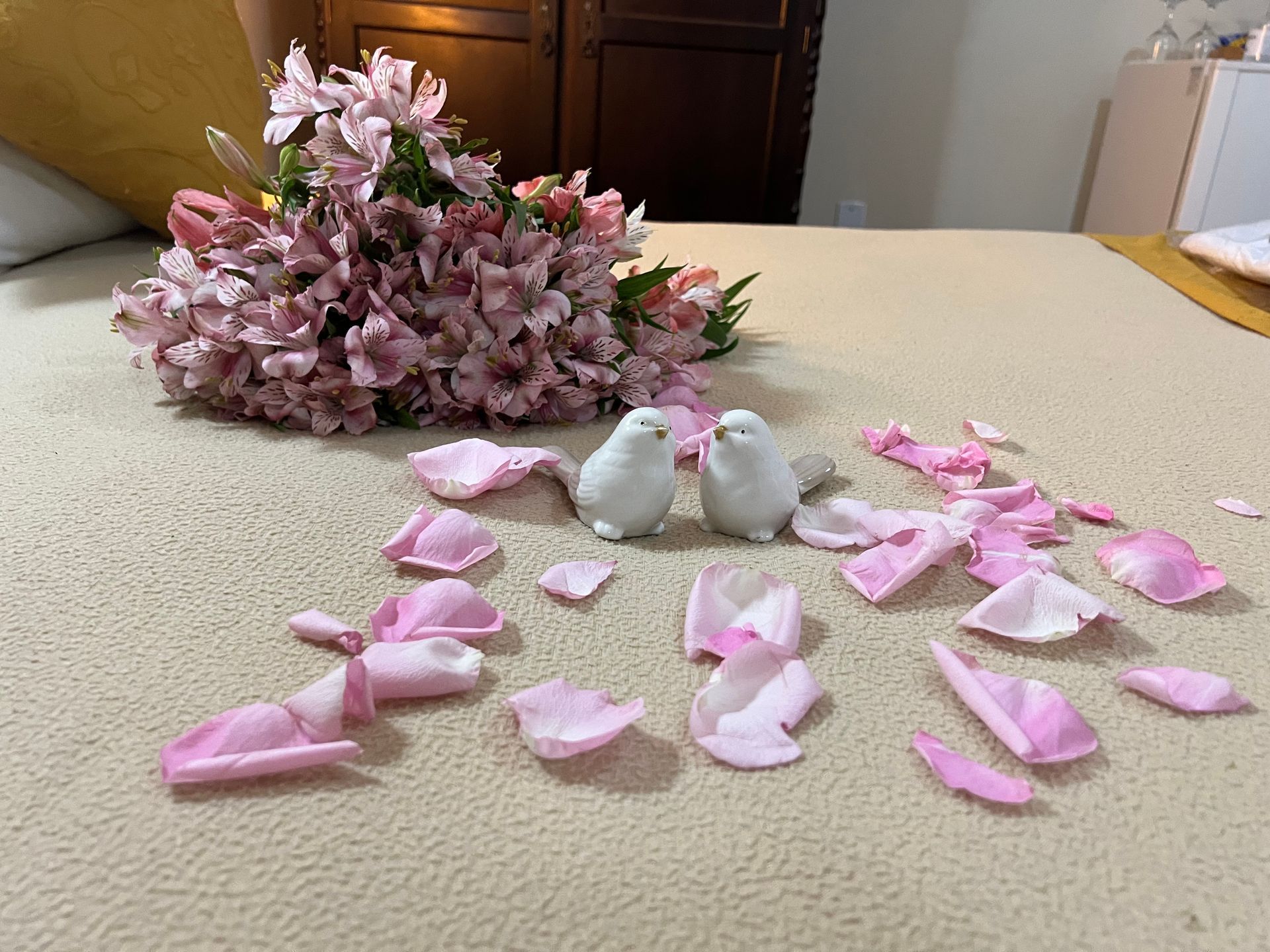 Flores cor-de-rosa espalhadas ao redor de dois pequenos pássaros brancos sobre uma mesa.