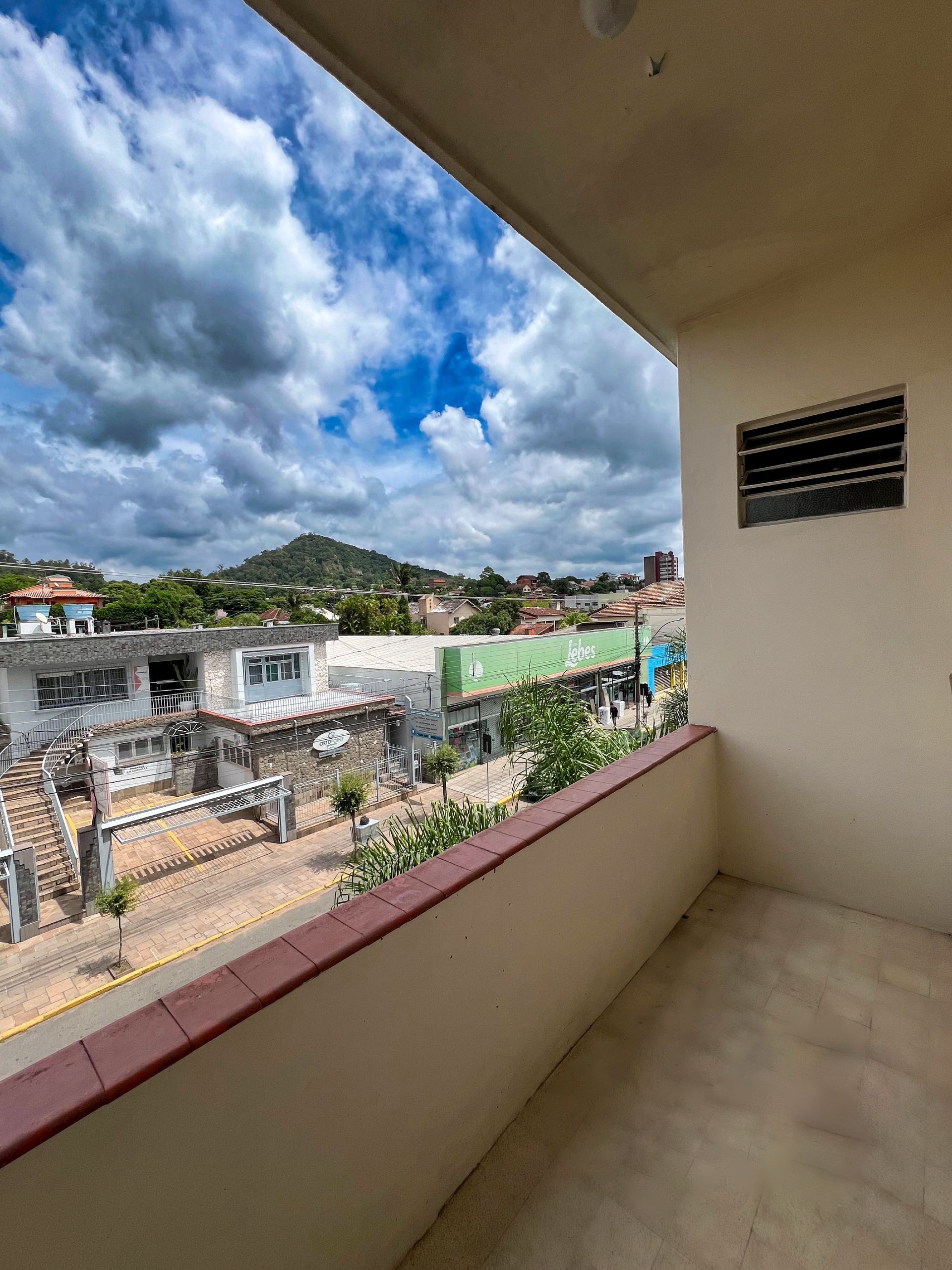 Varanda com vista para um bairro na encosta sob um céu azul nublado.