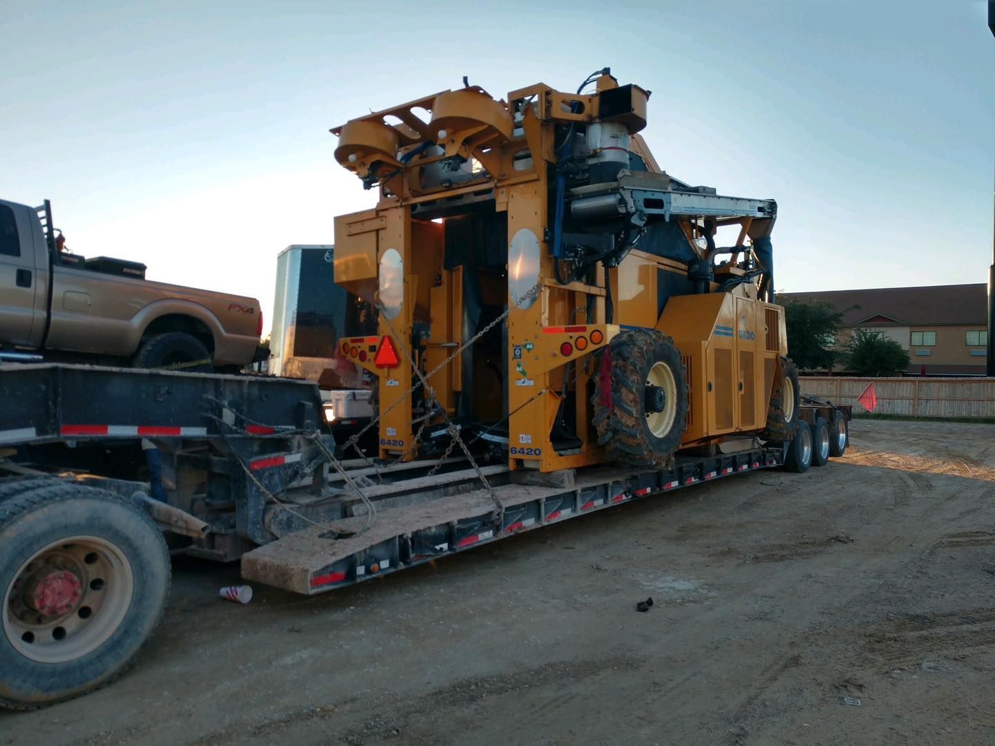 Yellow industrial machine on a flatbed trailer, in an outdoor setting.