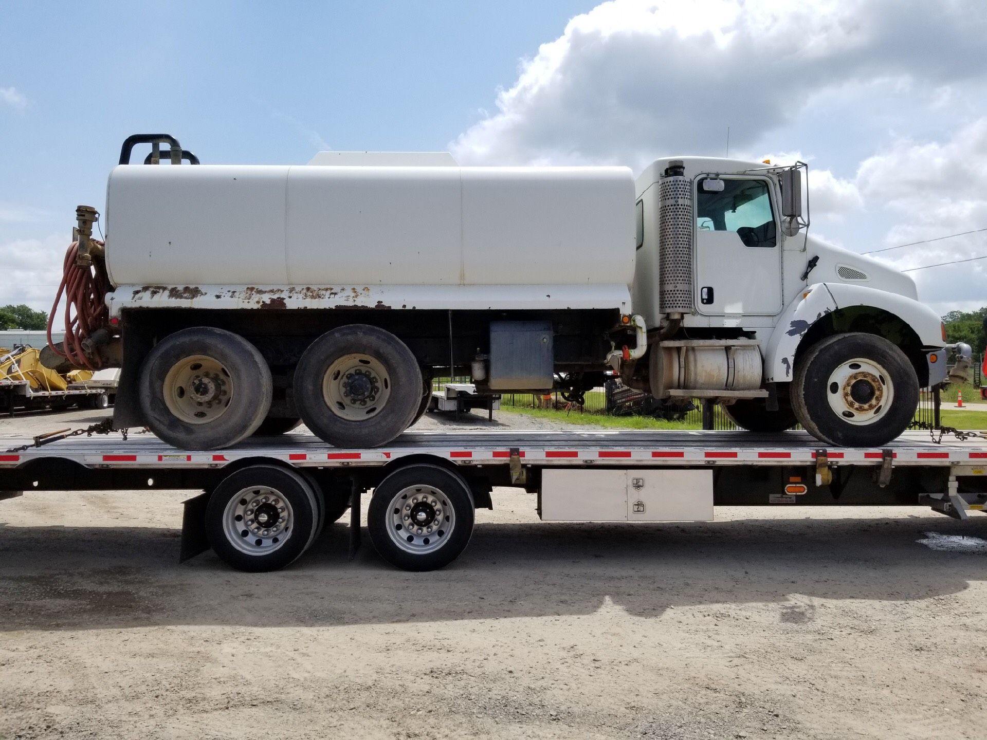 White water truck on a flatbed trailer, parked outdoors on gravel.