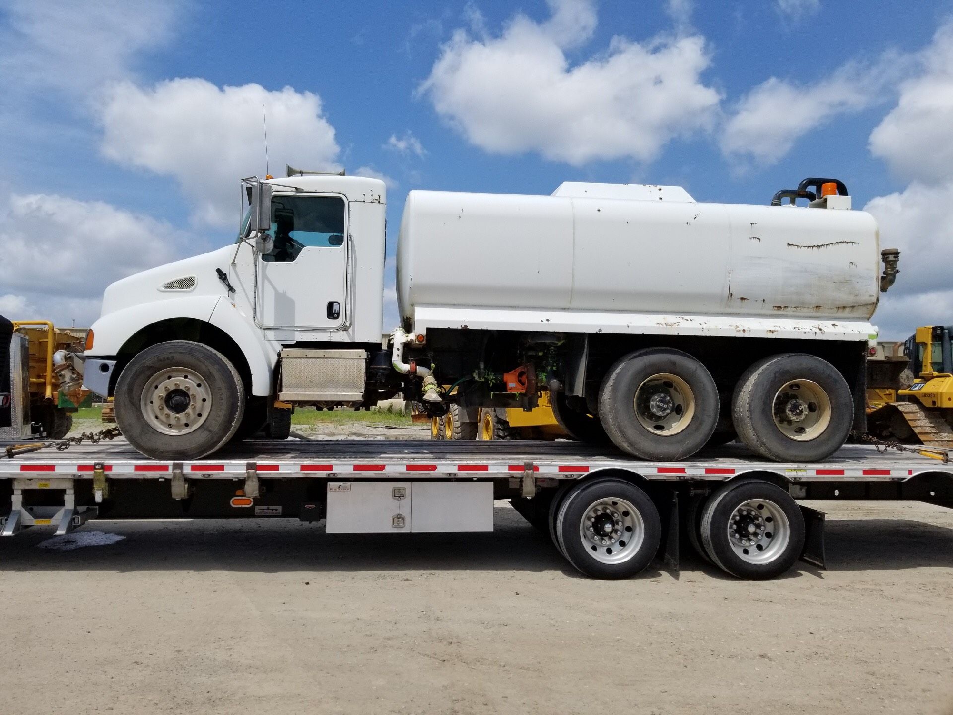 White water tanker truck on a trailer under a blue sky.