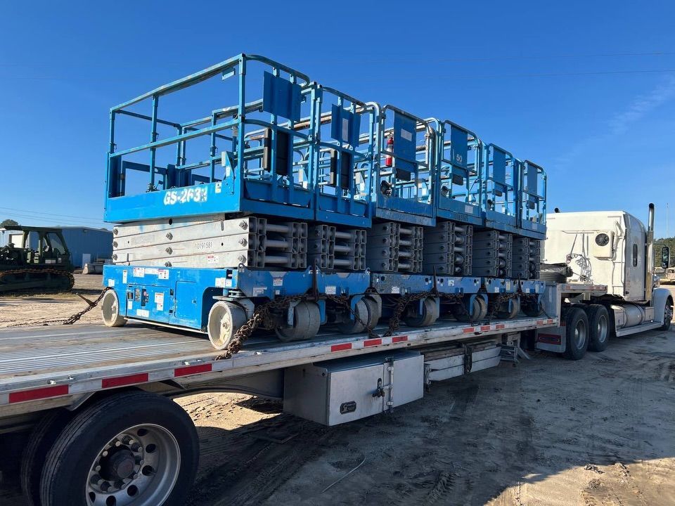 Blue scissor lift machinery secured on a flatbed trailer at a construction site