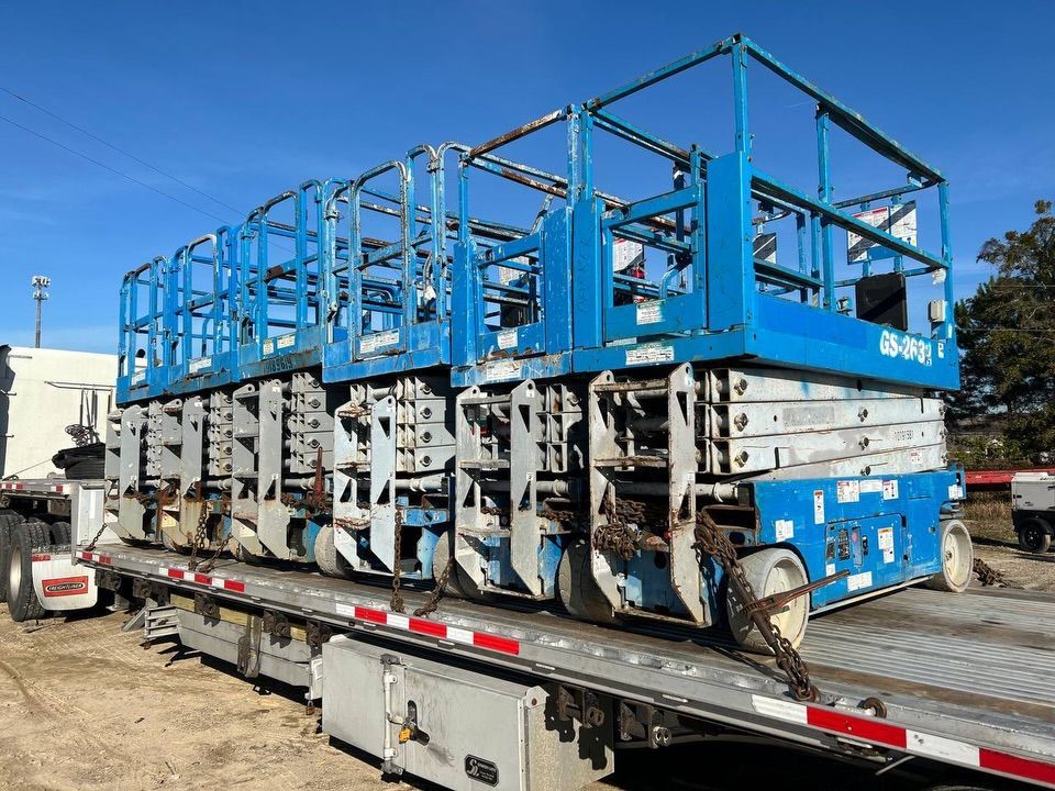 Blue industrial carts stacked on a flatbed trailer in a yard under a clear sky