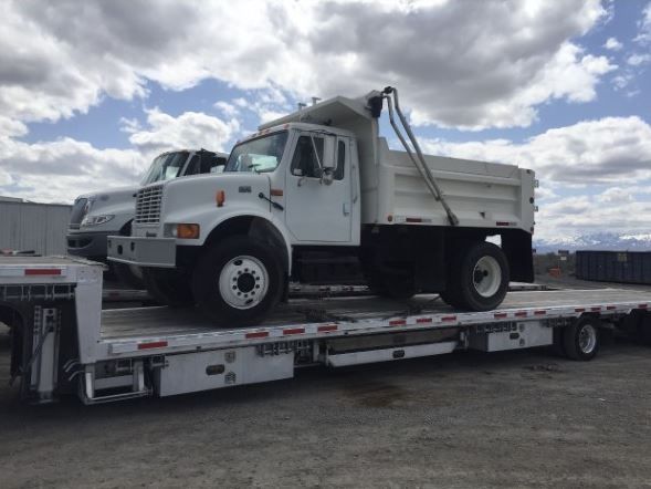 White dump truck on a flatbed trailer under a cloudy sky.