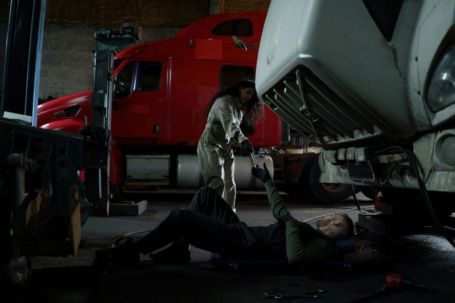 A man and a woman are working on a semi truck in a garage.