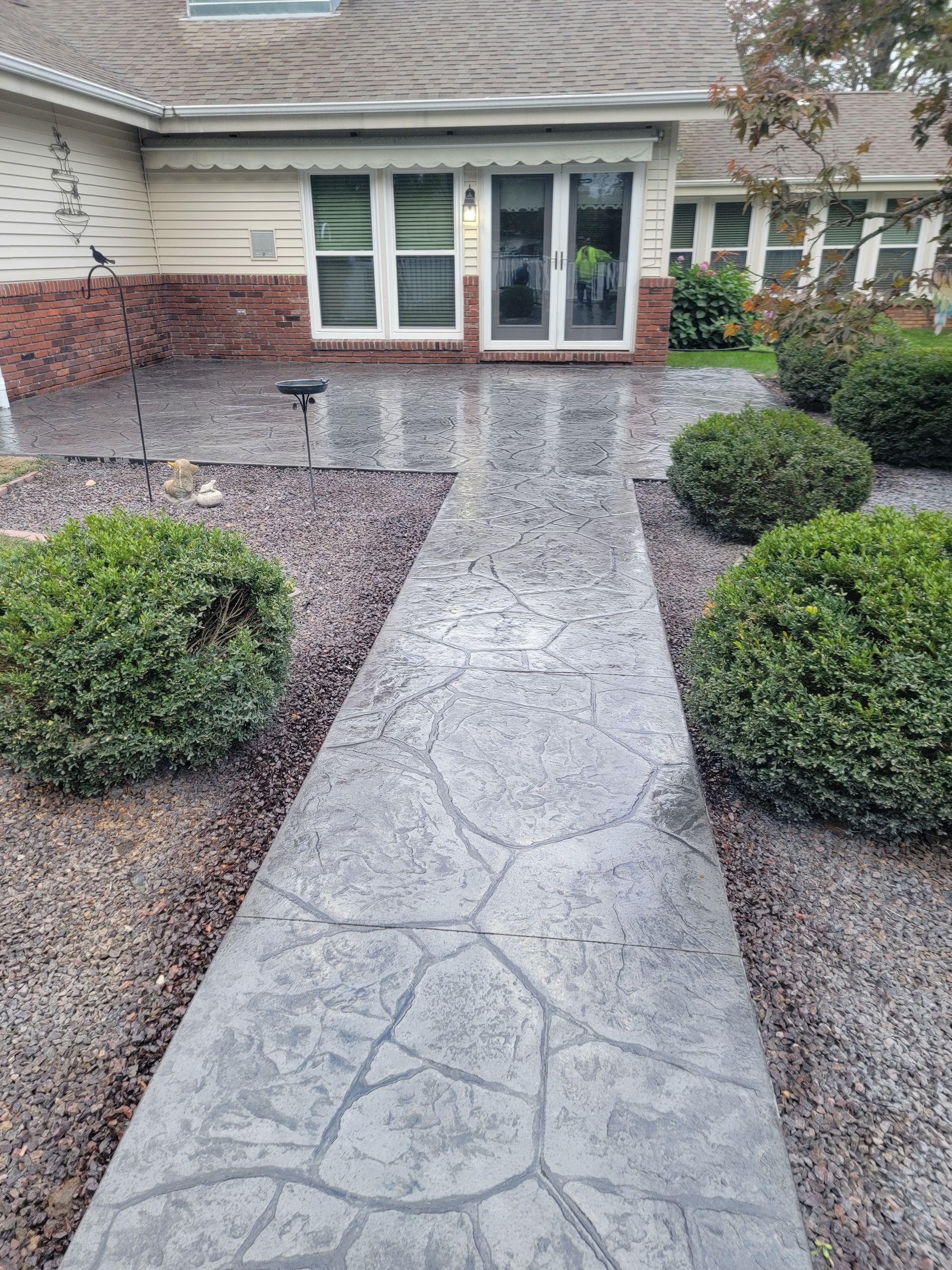 a concrete walkway leading to a house surrounded by bushes and gravel .