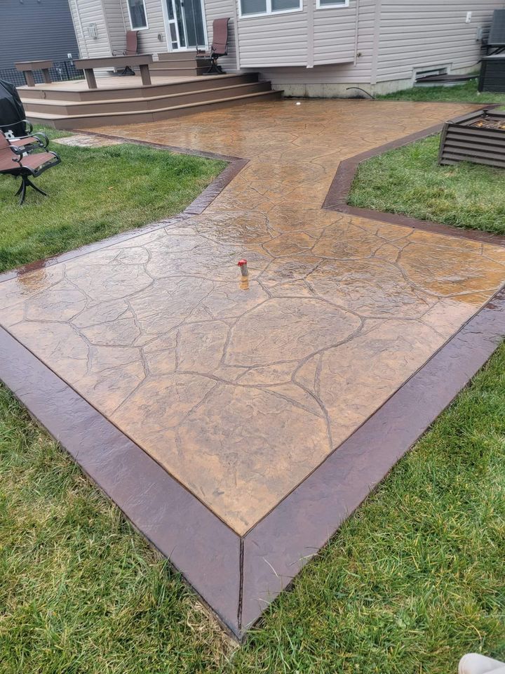 a stamped concrete patio to look like wood with a brick wall and a house in the background .