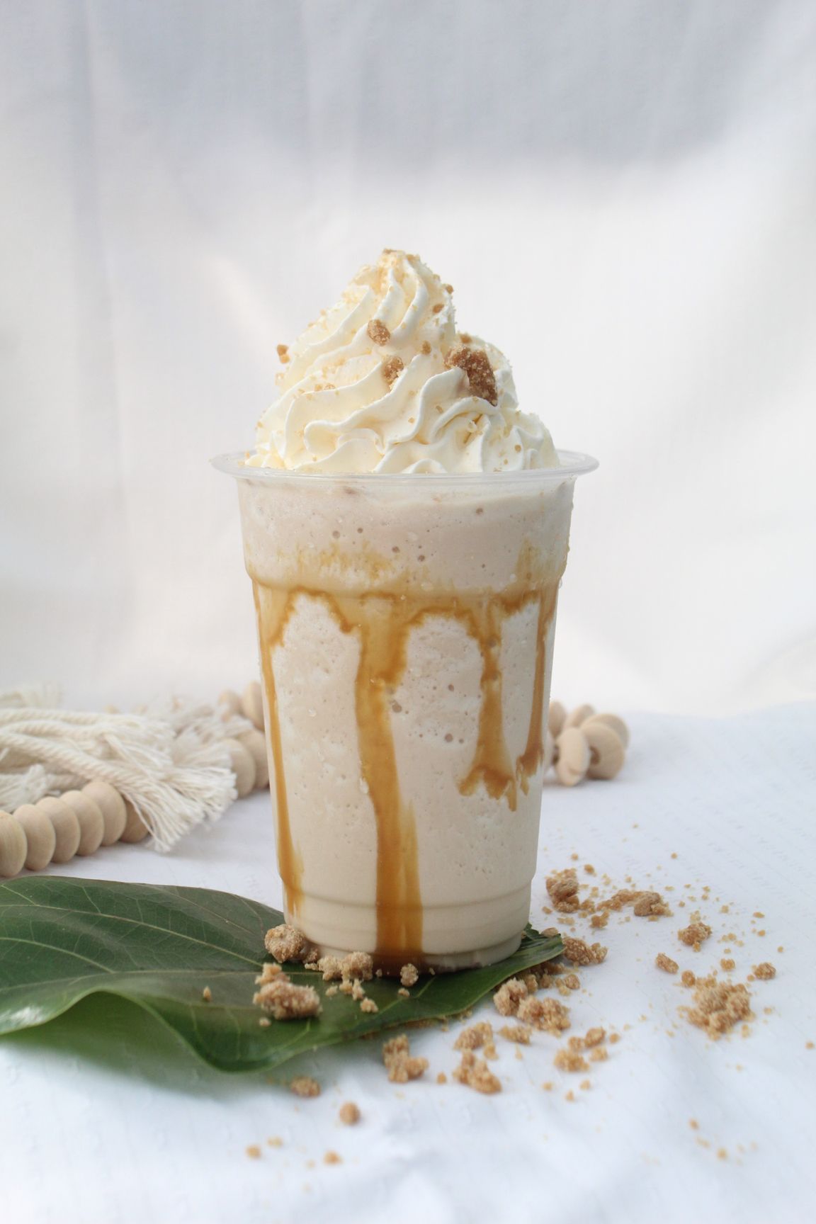 Iced coffee drink with cinnamon on top, next to pumpkins and yellow flowers on black.