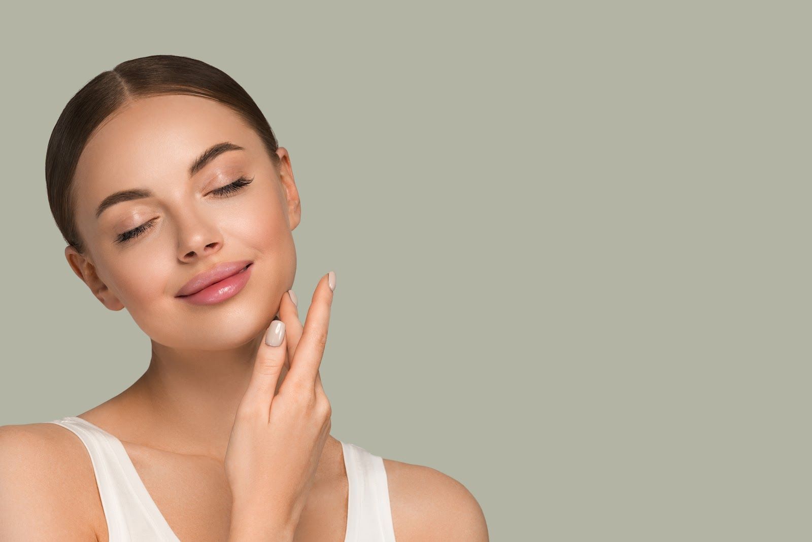Woman with closed eyes gently touching her cheek against a beige background