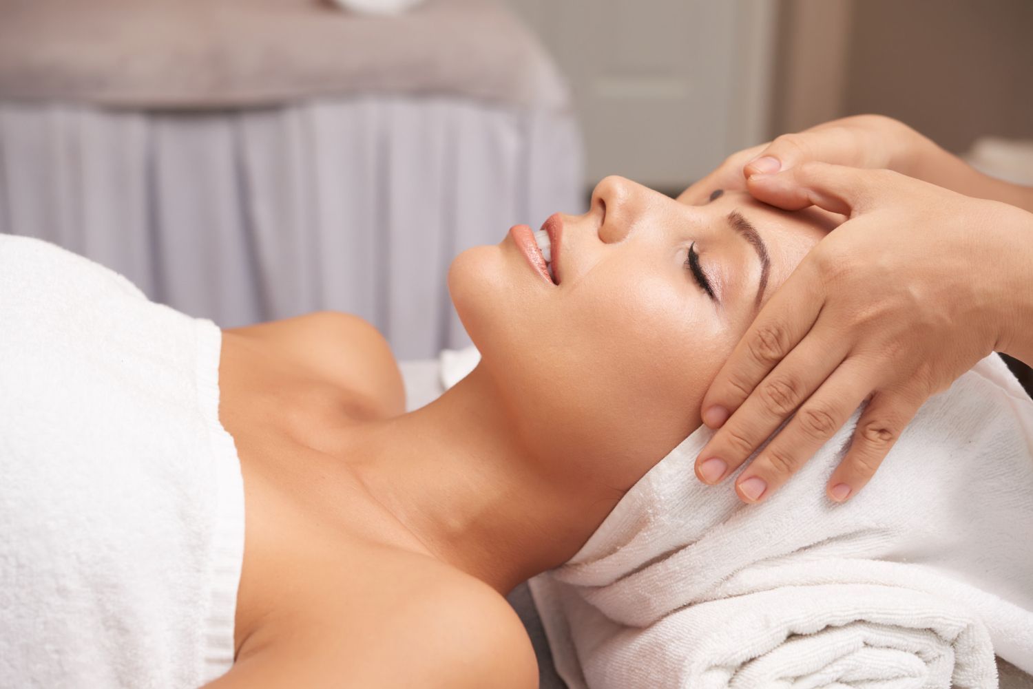 Woman receiving a facial massage while lying on a towel in a spa setting