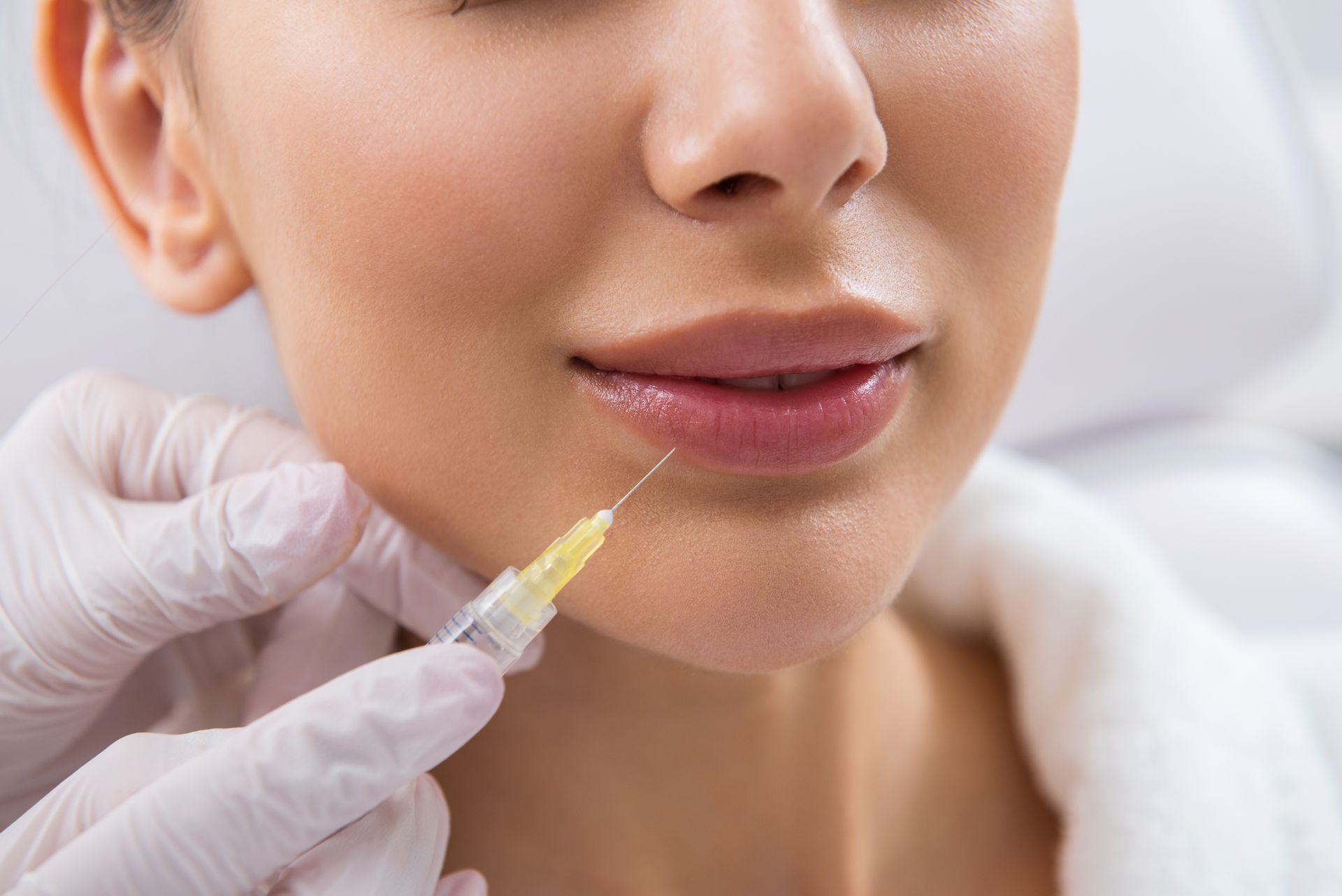 Gloved hand holding a syringe near a woman’s lips during a cosmetic injection procedure