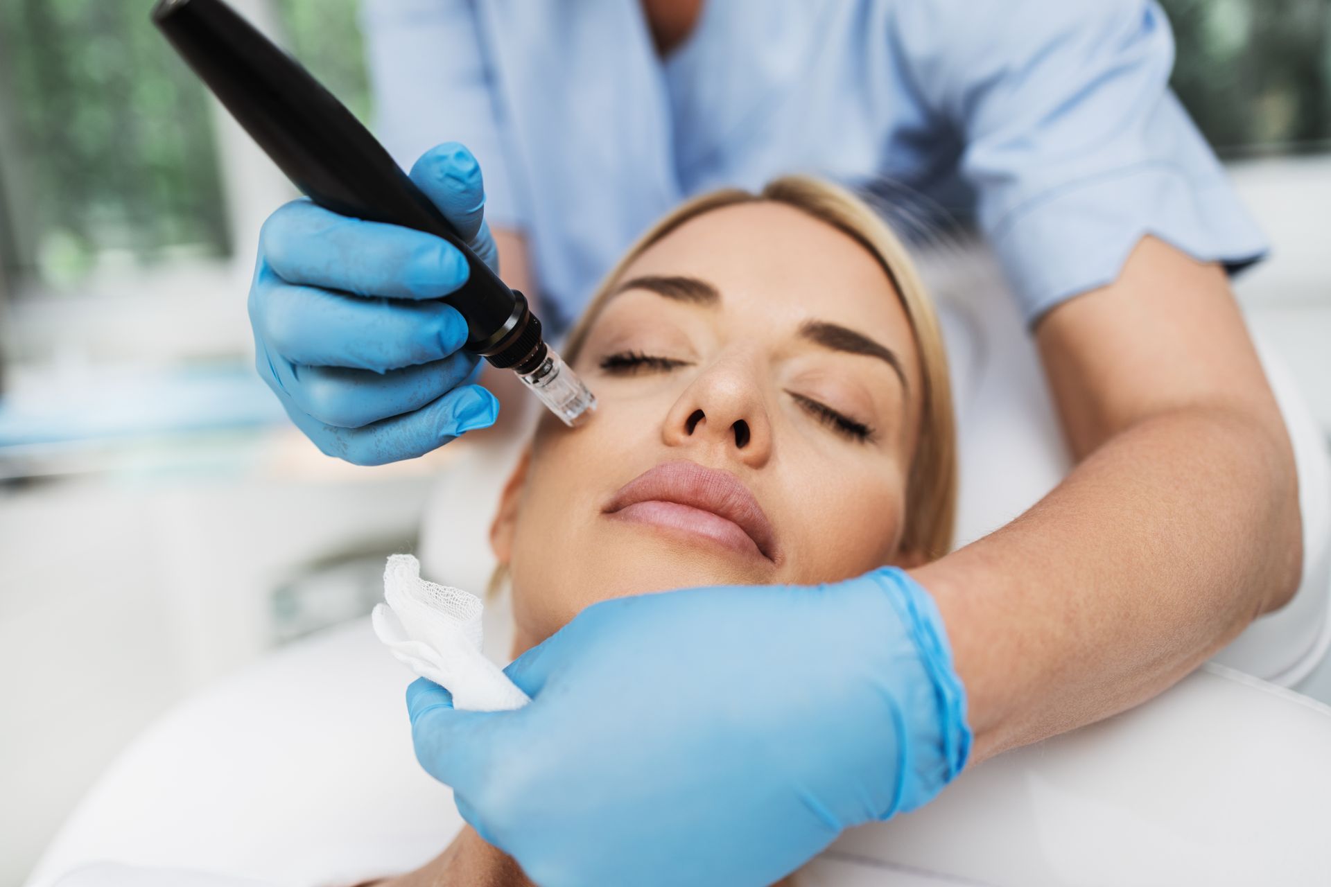 Cosmetic treatment in progress: gloved practitioner applies a facial device to a relaxed client.