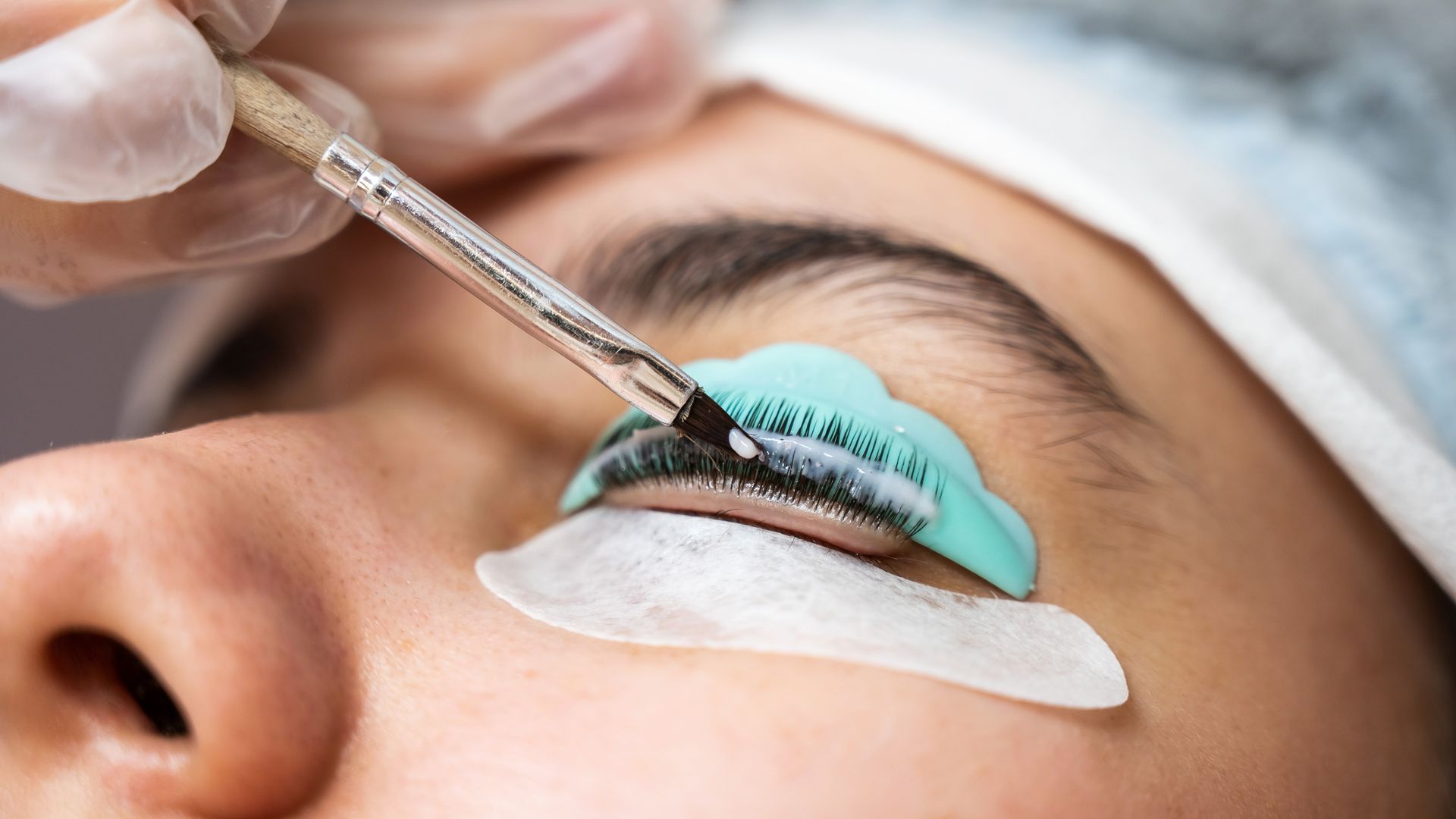 Applying lash lift treatment to a person's eye using a brush and blue curling shield.