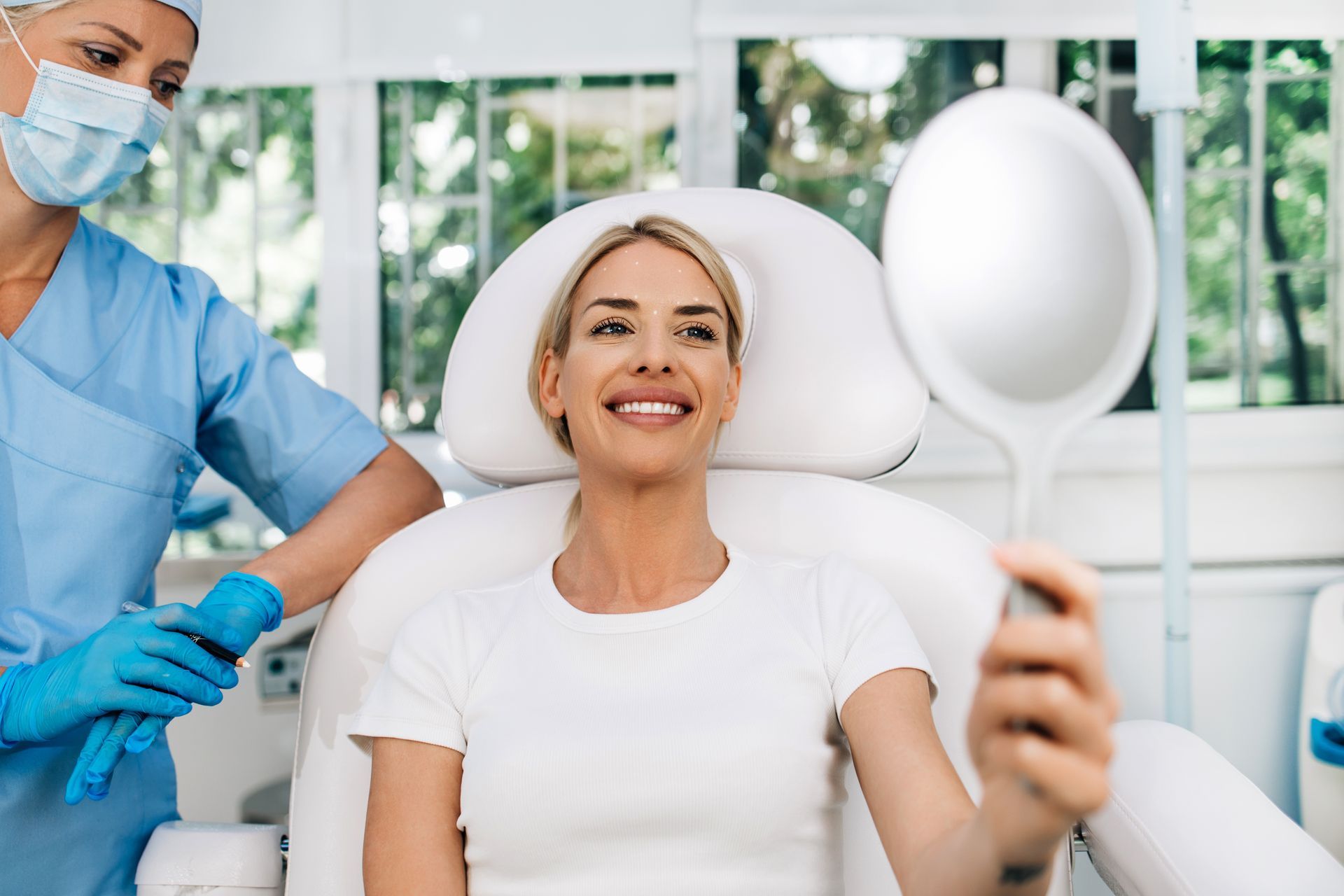 Patient smiling for a selfie in a bright dental clinic while a masked clinician stands beside her