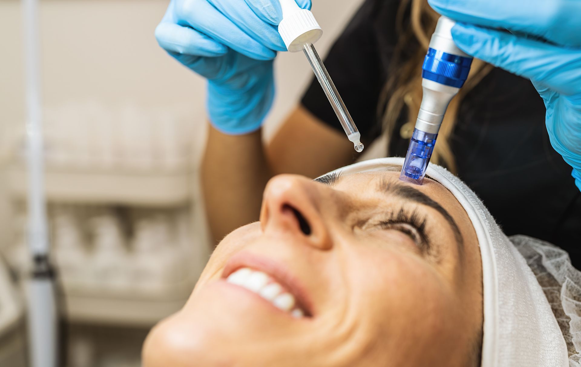 Woman receiving a microneedling treatment on her forehead; a technician drips serum.