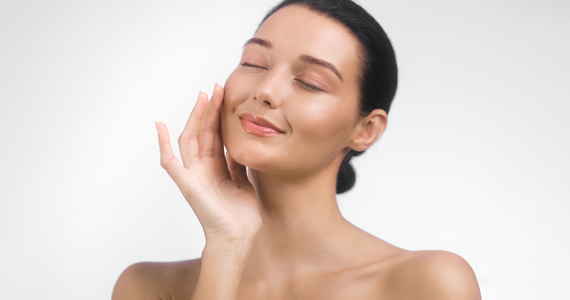 Woman with eyes closed, touching her cheek, against a white background.