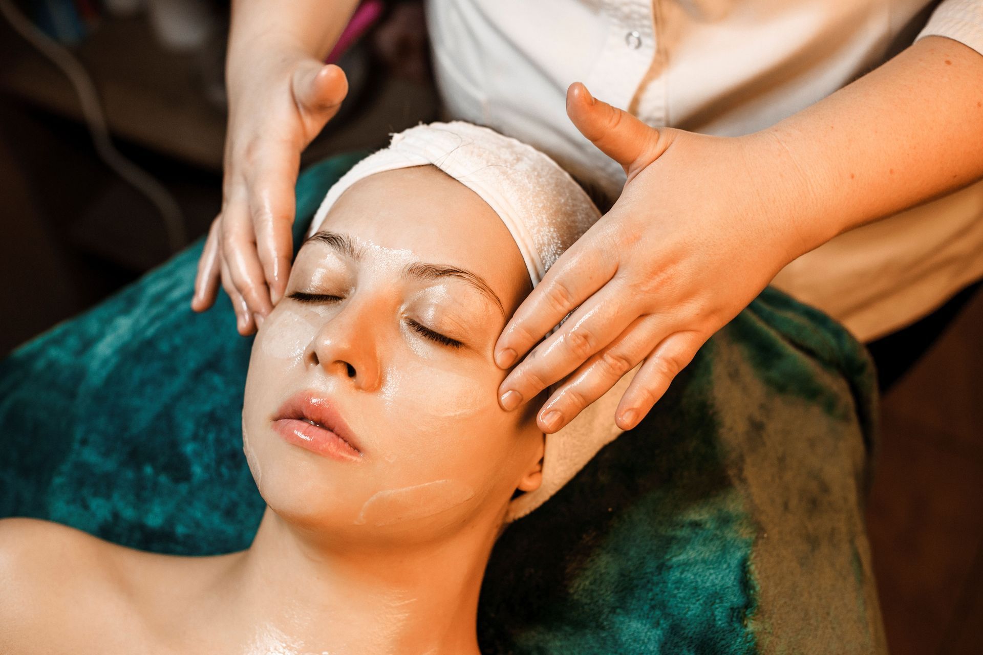 Facial massage in a spa, with hands on a woman’s face and a towel wrapped around her head