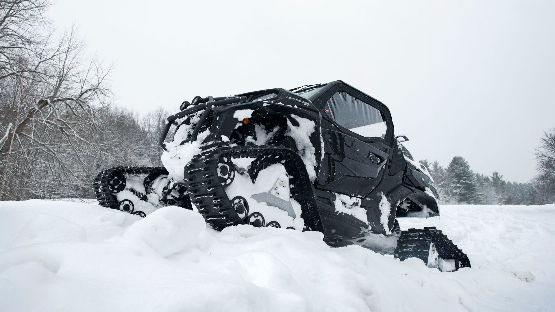 Veicolo cingolato nero che avanza nella neve alta in un paesaggio invernale.