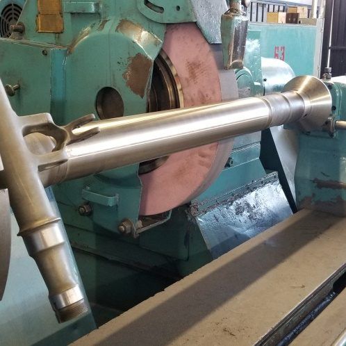 A cylindrical metal part being ground on a large industrial grinding machine.