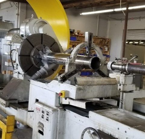 A large industrial lathe machine with a metal cylindrical object being worked on.