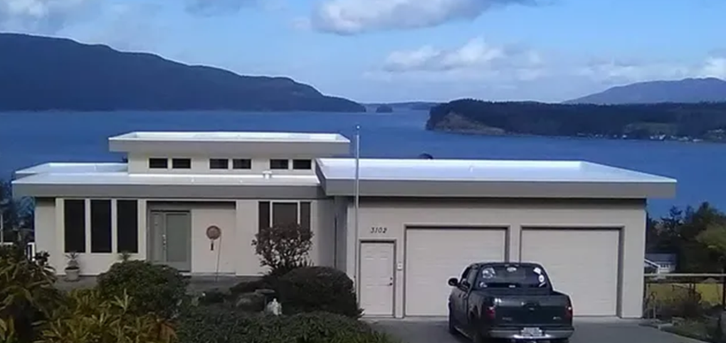 A truck is parked in front of a house with a view of the ocean.