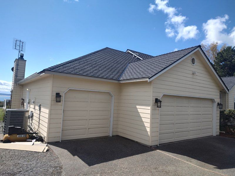 A white house with a black roof and two garage doors