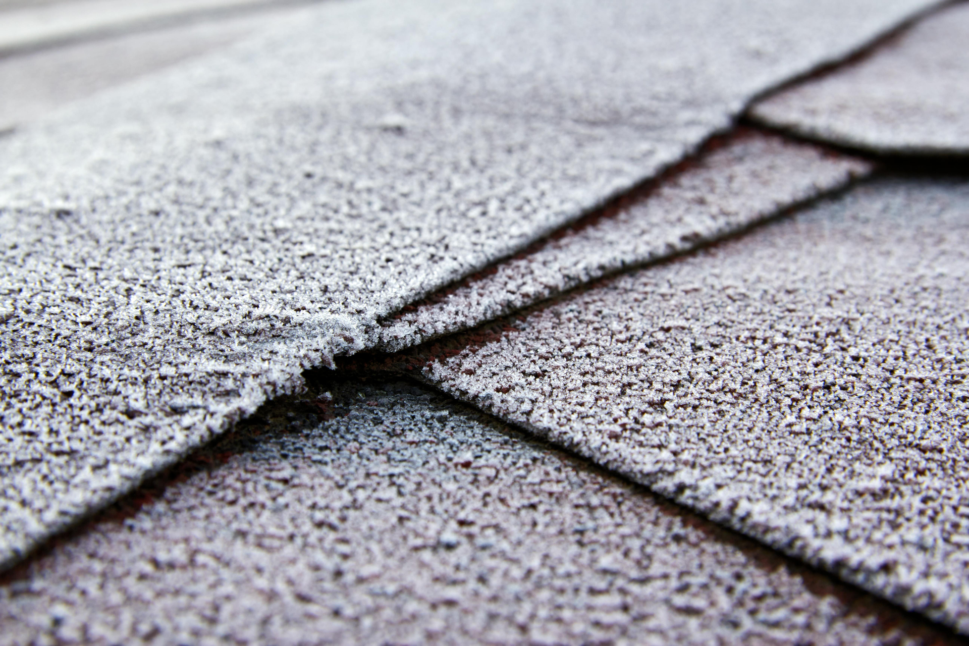 Frost covers overlapping brown roof shingles.