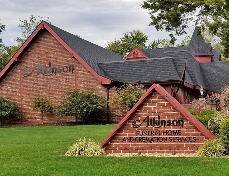 Red brick Atkinson Funeral Home and Cremation Services building with a sign on green grass.