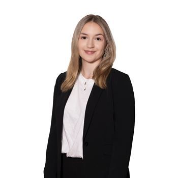 A professional portrait of a person with shoulder-length blonde hair, wearing a white shirt under a black blazer.