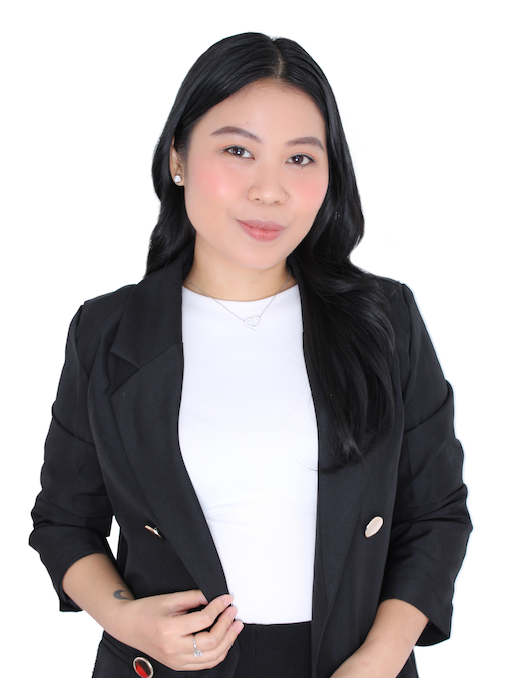 A person with long dark hair, wearing a black blazer over a white shirt, stands against a plain white background.
