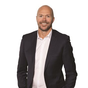 A smiling man wearing a white shirt and dark blue blazer, posed against a solid white background.