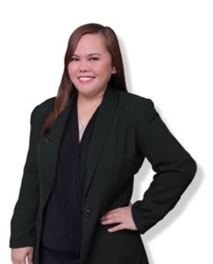 A person with long brown hair smiling, wearing a dark blazer over a black top, standing with one hand on their hip.