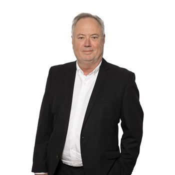 A man in a black blazer and white dress shirt posing against a plain white background.